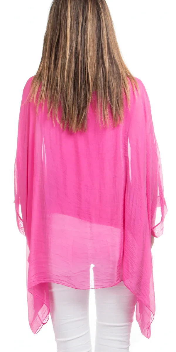 Back view of woman wearing sheer hot pink poncho top with white pants