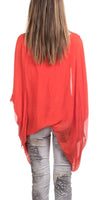 Back view of woman in sheer red poncho top and patterned grey pants