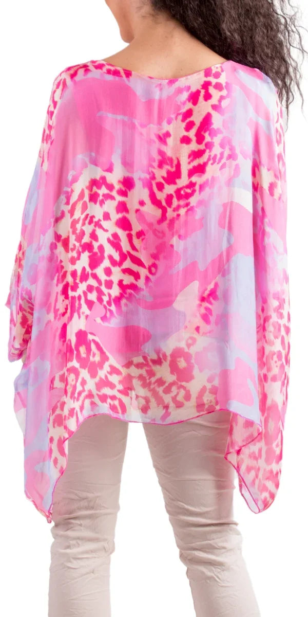 Woman wearing sheer pink animal print poncho top with light pants, photographed from the back