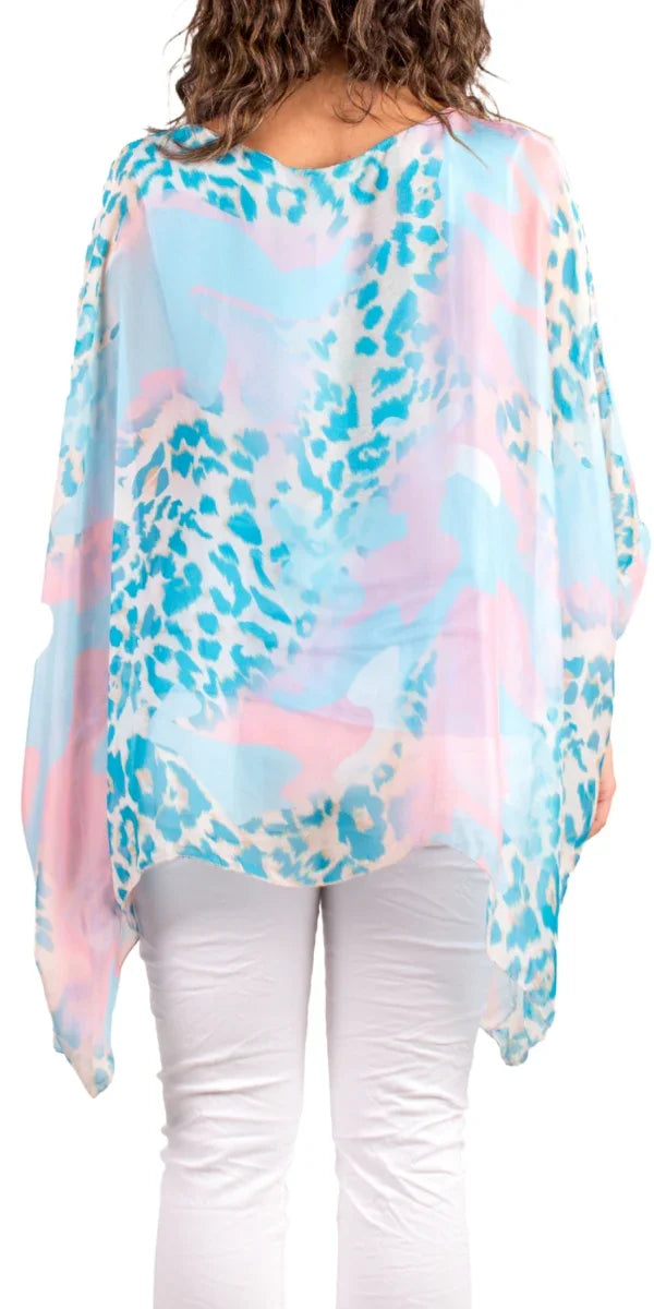 Back view of woman wearing pastel blue and pink animal print sheer poncho top with white pants