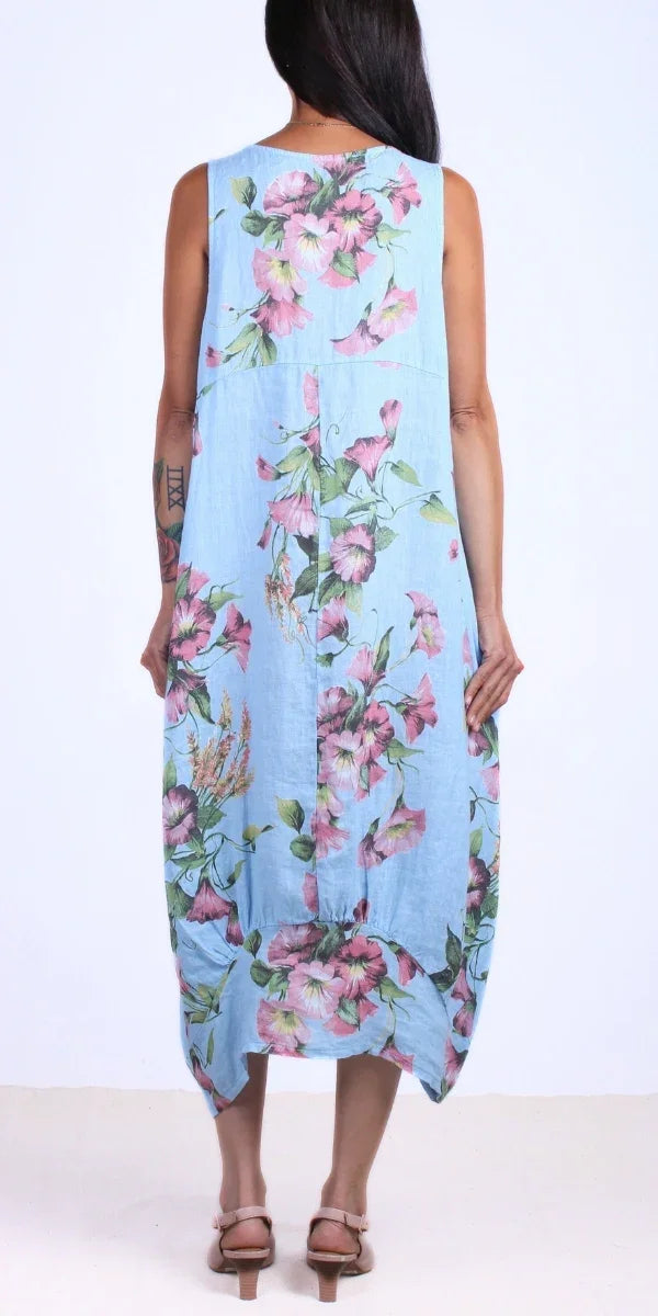 Woman wearing a sleeveless light blue floral linen dress, shown from the back, with sandals