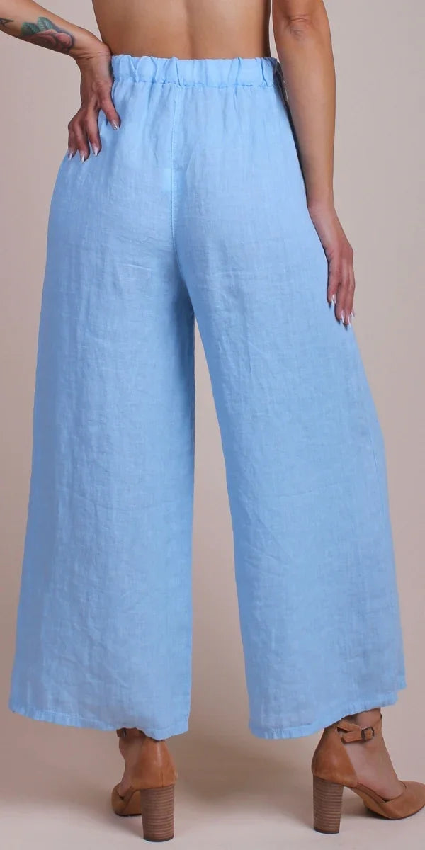 Back view of woman wearing light blue wide-leg linen pants and brown heel sandals