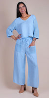 Woman wearing a light blue linen pants set with crochet sleeves and pocket details