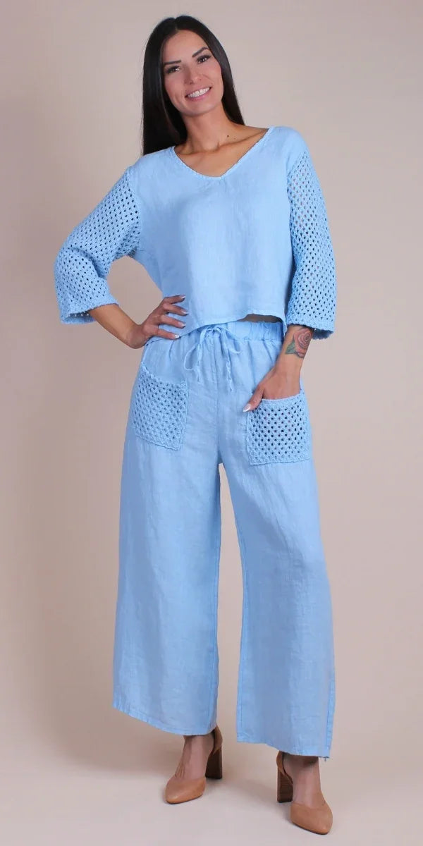 Woman wearing a light blue linen pants set with crochet sleeves and pocket details