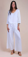 Woman wearing white linen pants and top with crochet sleeves and pockets, neutral background
