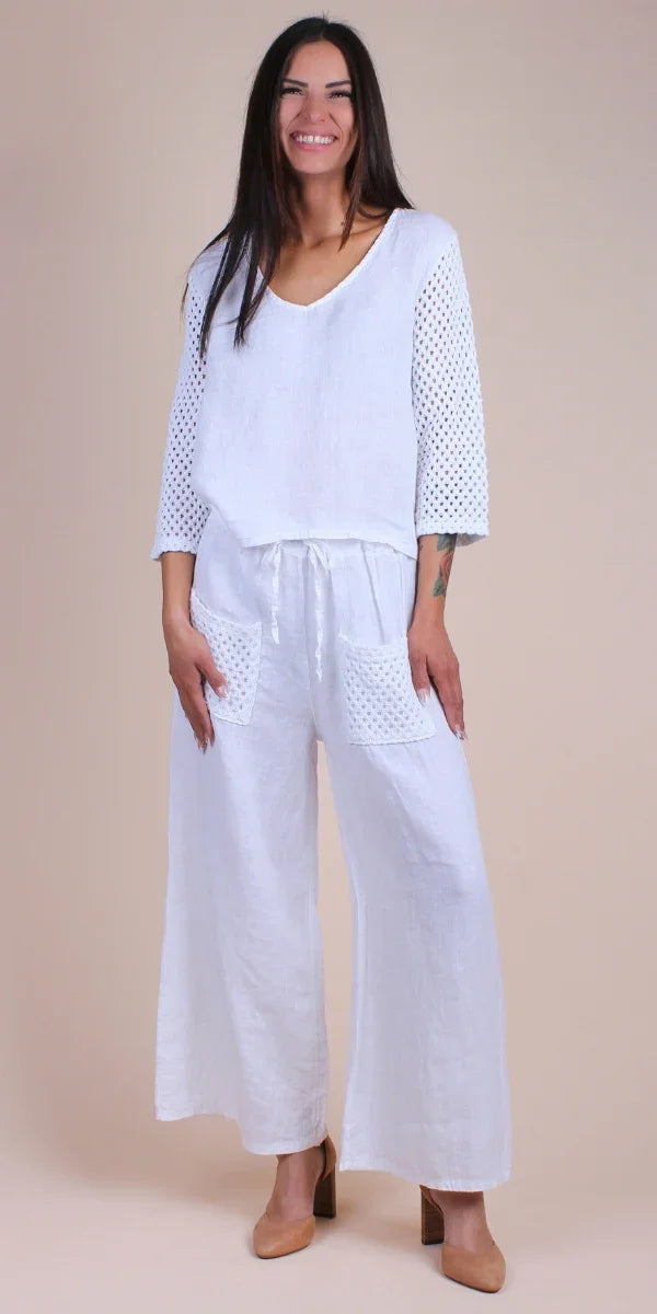 Woman wearing white linen pants and top with crochet sleeves and pockets, neutral background