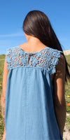 Woman in blue sleeveless dress with lace crochet back, standing outdoors on a sunny day