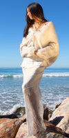 Woman in cream knit cardigan and lace silk skirt on beach rocks by the ocean