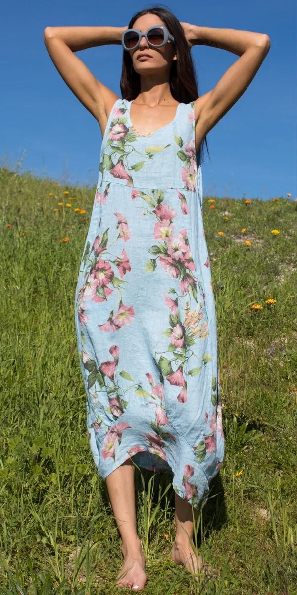 Woman in blue floral linen dress and sunglasses standing barefoot in grassy field