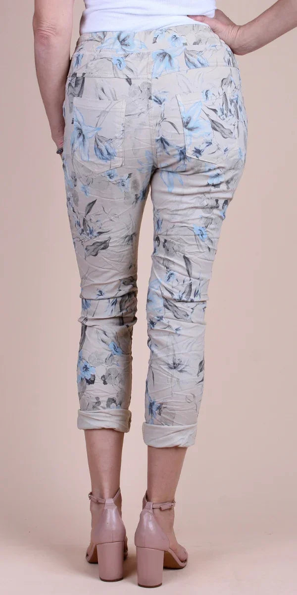 Back view of cropped floral print pants in beige with blue accents, paired with block heel sandals
