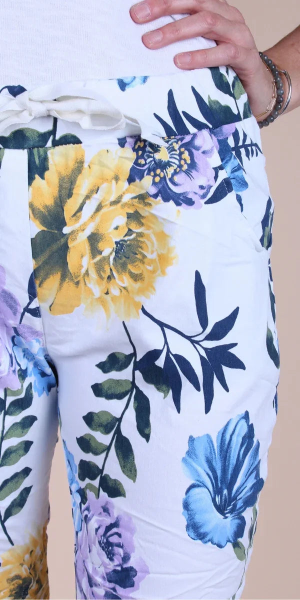 White floral print pants with yellow, blue, and purple flowers, linen texture, woman’s hand on waist