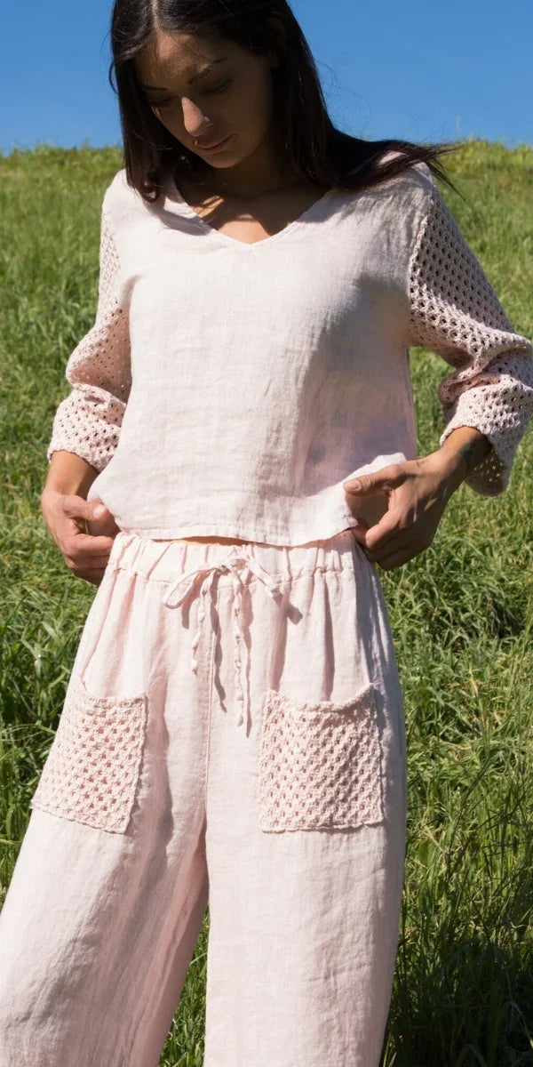 Woman wearing light pink linen set with crochet sleeves and pockets in outdoor field