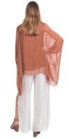 Woman wearing sheer brown poncho top and wide-leg white pants, back view