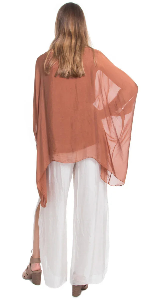Woman wearing sheer brown poncho top and wide-leg white pants, back view
