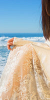 Woman in cream knit sweater and floral lace skirt by the ocean on a sunny day
