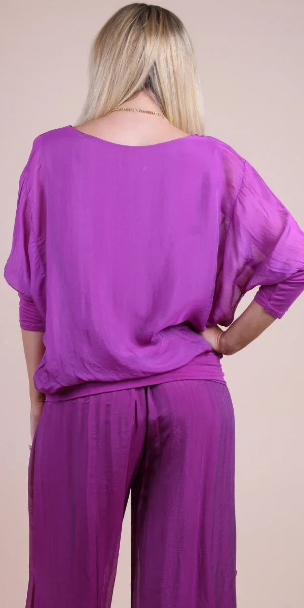Woman wearing purple silk top and matching wide-leg pants, photographed from the back