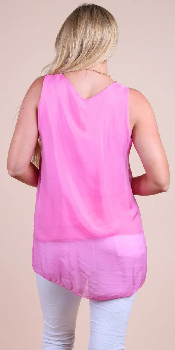 Woman wearing a sleeveless pink silk tunic top and white pants, back view