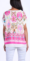 Back view of woman wearing a white top with pink, gold, and blue baroque print and white pants