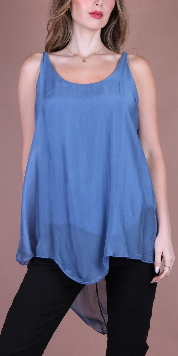Woman wearing a flowy blue silk tank top with a high-low hem, paired with black pants
