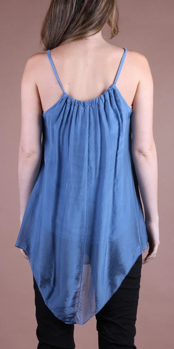 Woman wearing a flowy blue silk tank top with a high-low hem, paired with black pants