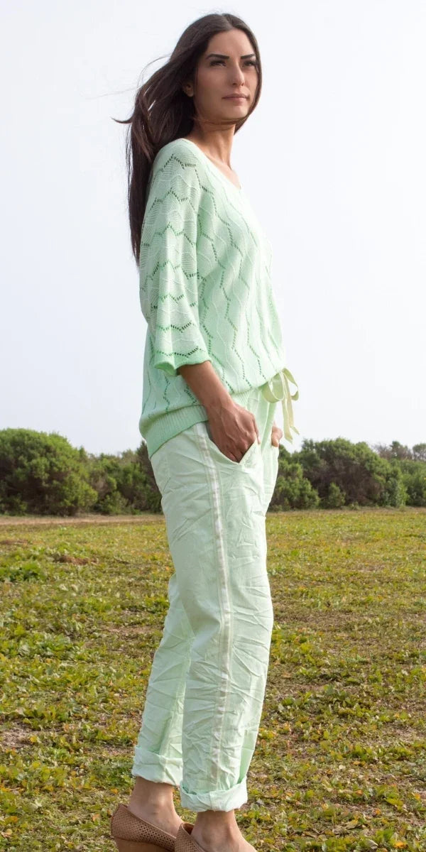 Woman wearing light green knit top and matching linen pants outdoors on grass