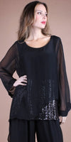 Woman wearing a sheer black long-sleeve blouse with sequin details and black pants