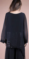 Back view of a woman wearing a black sheer tunic with sequin details and wide sleeves