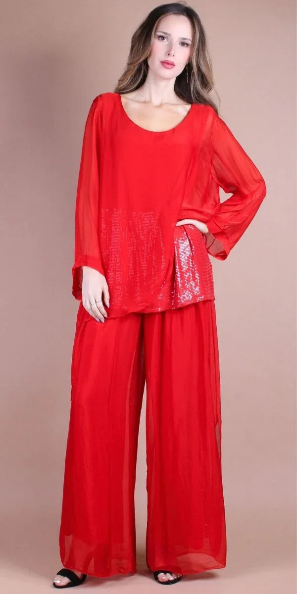 Woman wearing red sheer blouse with sequin detail and wide-leg red pants, neutral background