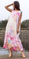 Woman in sleeveless white maxi dress with pink floral print, standing by a lakeside dock