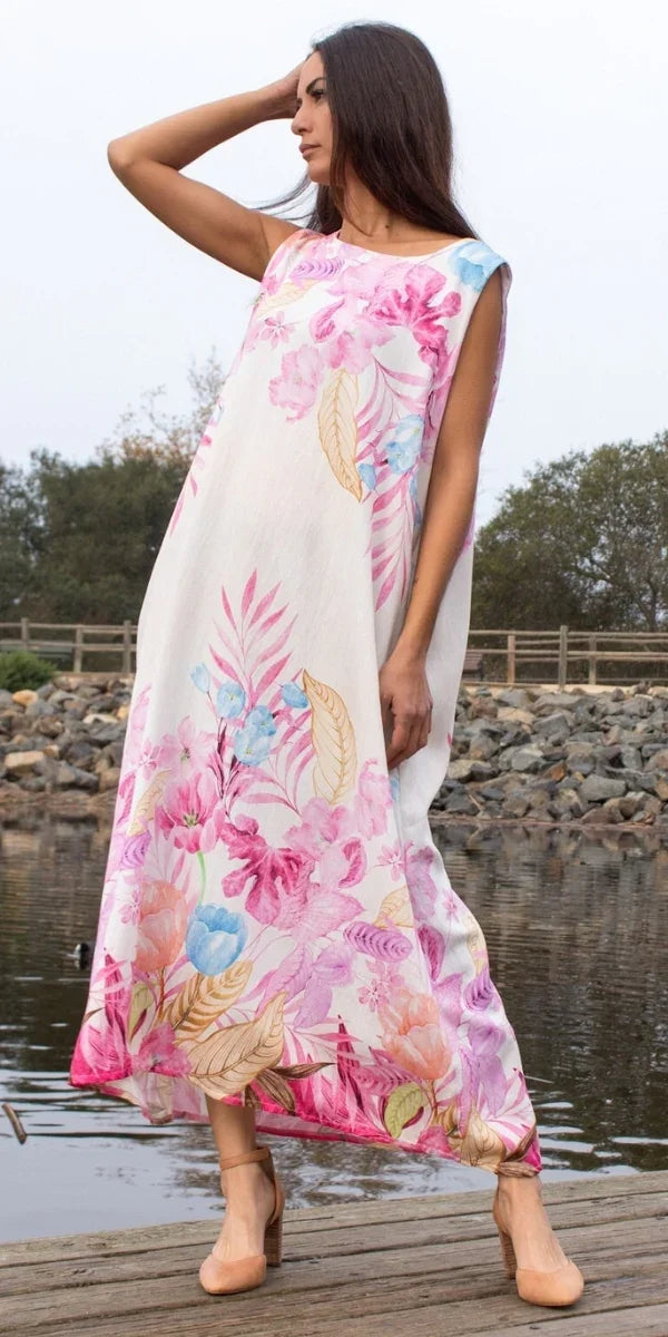 Woman in sleeveless white maxi dress with pink floral print, standing by a lakeside dock