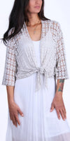 Woman wearing a white openwork lace cardigan with tie front over a white dress