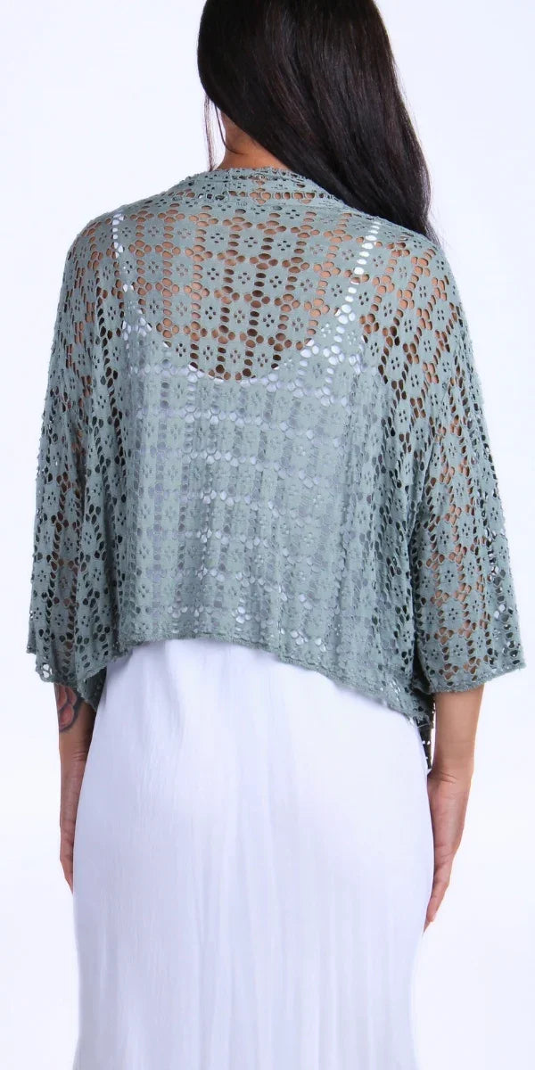 Woman wearing sage green open-knit crochet poncho over a white dress, back view