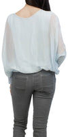Woman wearing a sheer light blue blouse and gray pants, shown from the back