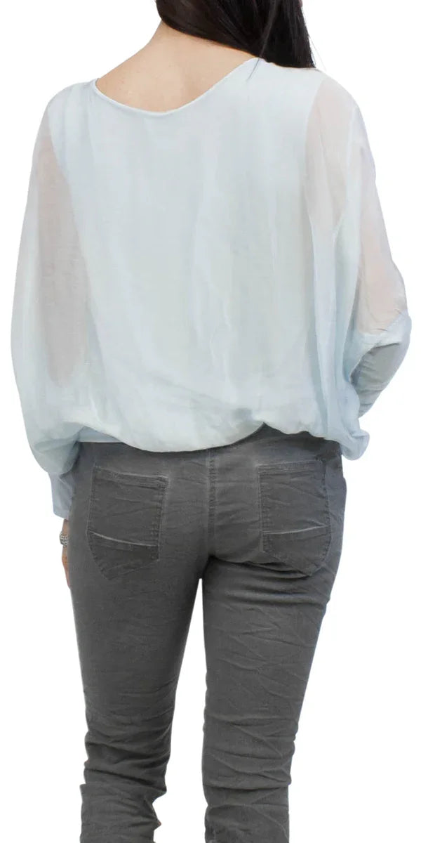Woman wearing a sheer light blue blouse and gray pants, shown from the back