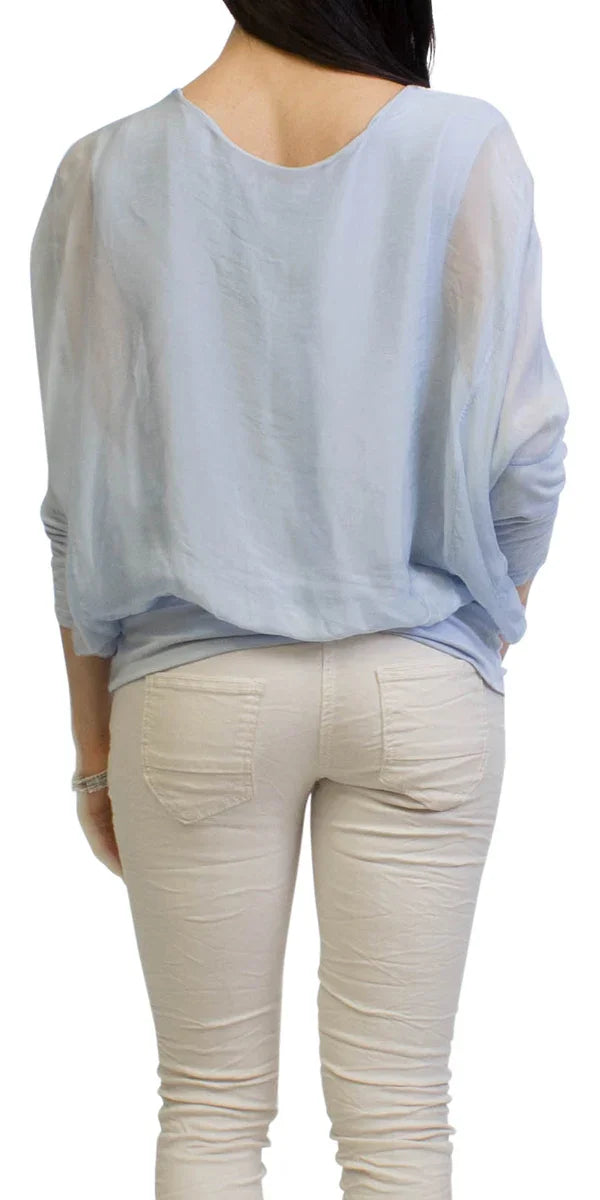 Woman wearing a sheer light blue blouse and beige skinny pants, shown from the back