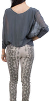 Woman wearing sheer dark gray blouse and beige snake print pants, back view