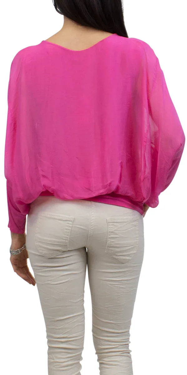 Woman wearing a vibrant pink sheer blouse with long sleeves and light beige pants, back view