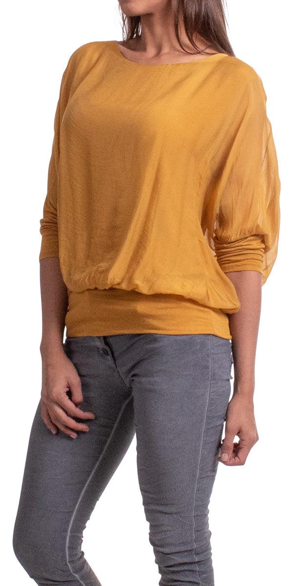 Woman wearing a loose mustard yellow blouse with dolman sleeves and grey jeans