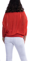 Woman wearing red sheer blouse with dolman sleeves and white pants, back view
